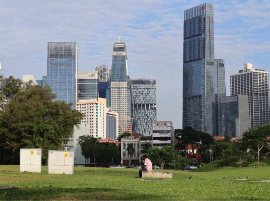 A migrant worker rests in a barren field against the backdrop of Singapore’s financial district.