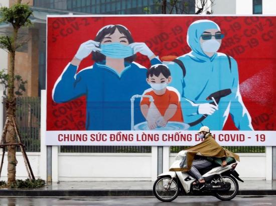 A man on a motorcycle drives past a Covid-19 fight poster in the capital city of Hanoi, Vietnam
