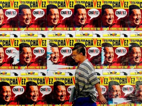man walks past wall covered in posters of Hugo Chavez