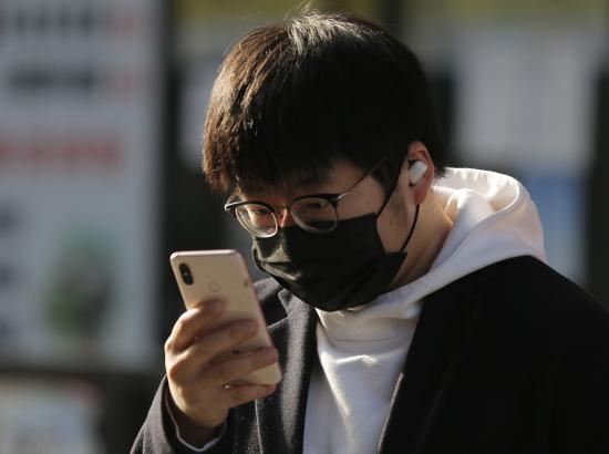 a man wearing protective face mask looks at his smartphone