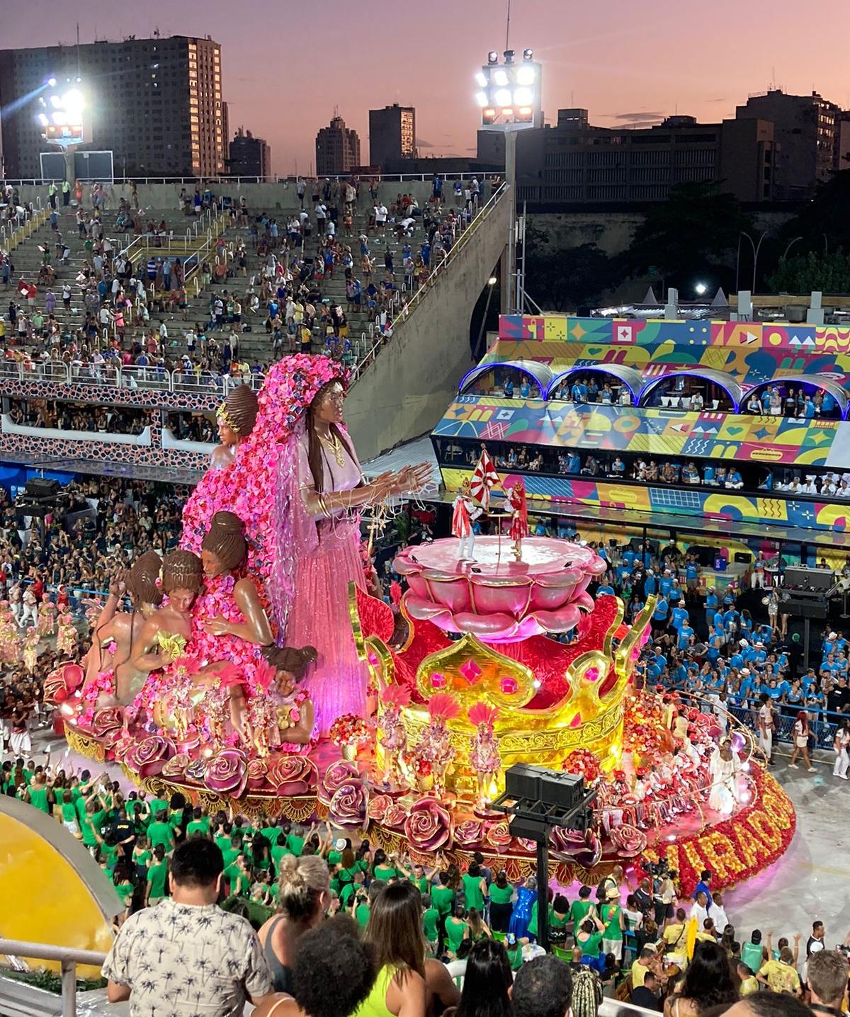 Rosa Maria in the In the parade’s last float, crowned a Saint, with her rosy mantle protecting other Black women.