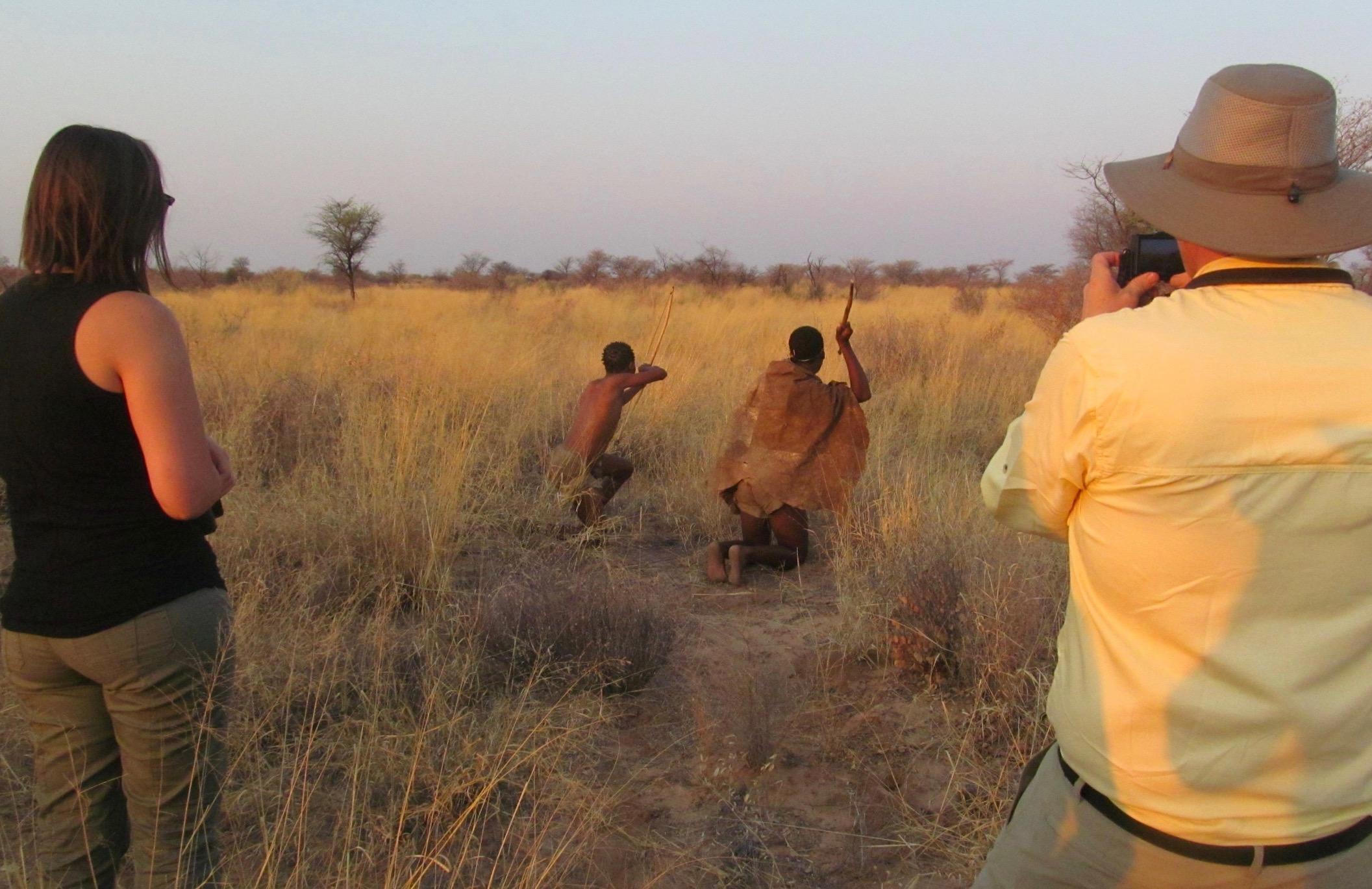 tourists take photo of hunting demonstration by two young San