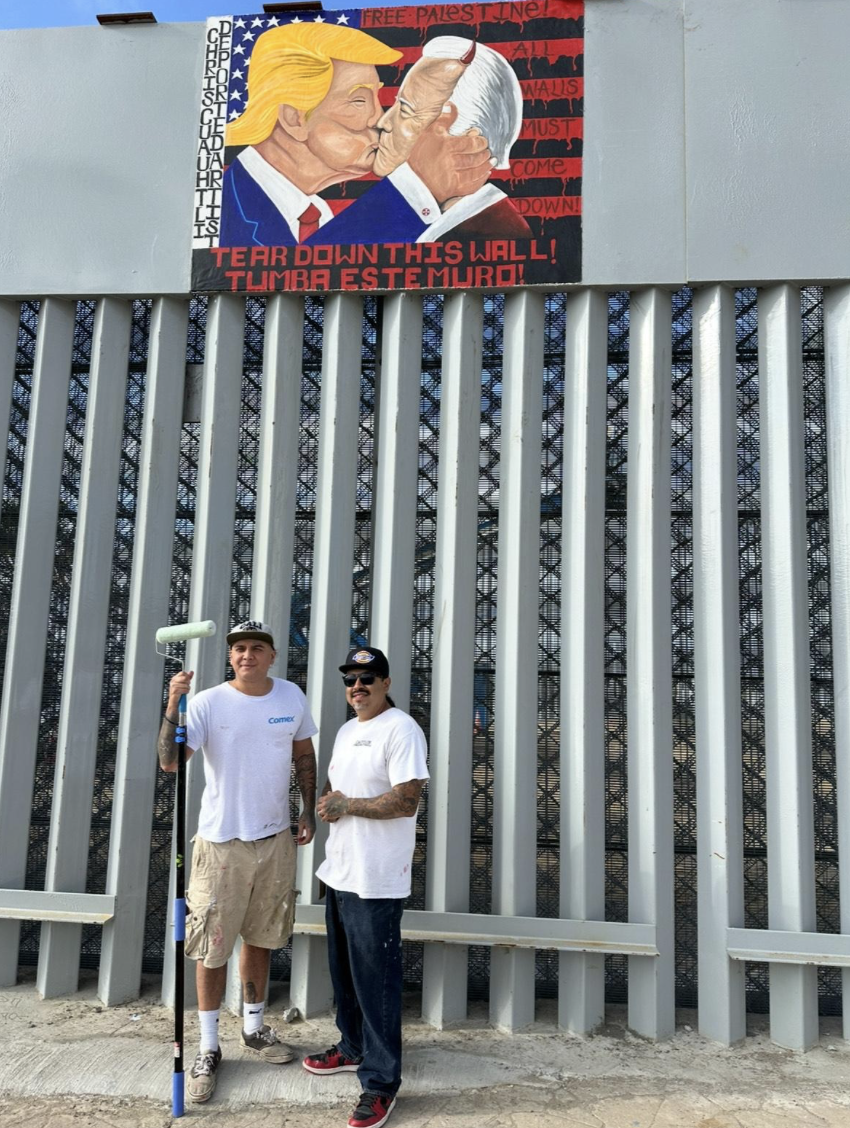Chris Cuauhtli (left) and Javier Salazar Rojas (right) stand beneath their revised mural of Trump and Biden at the newly-fortified border wall in Friendship Park, Tijuana, Mexico in March 2024. (Photo credit: Javier Salazar Rojas / @DeportedArtist)