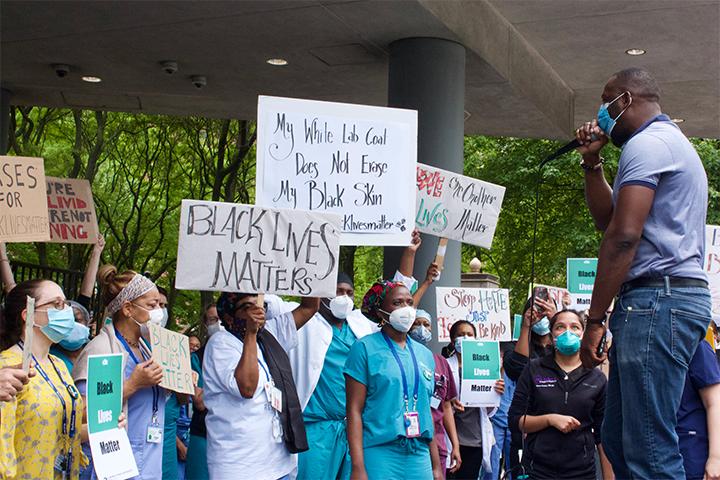 black healthcare workers in uniforms and masks protest George Floyd killing with signs and banners