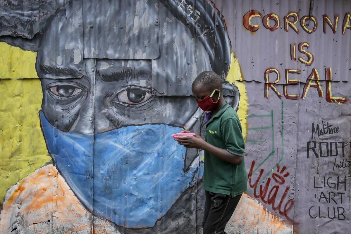 a boy wearing a face mask walks past an informational mural warning of the COVID-19 danger in Nairobi, Kenya