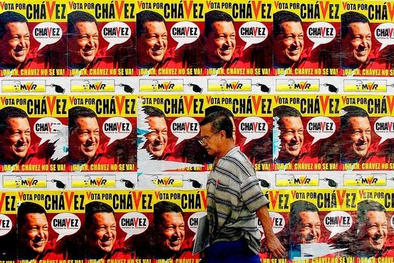 man walks past wall covered in Hugo Chavez posters