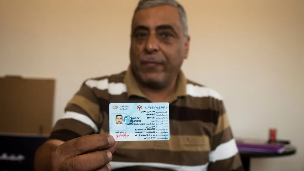 Jordanian farm owner holds up a work permit that he processed through the Ministry of Labour for one of his Syrian workers. 