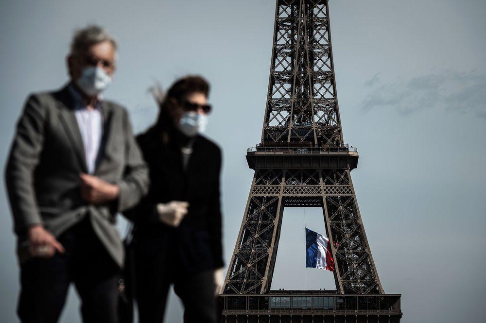 Pedestrians wearing facemarks walk past the Eiffel Tower in May 2020