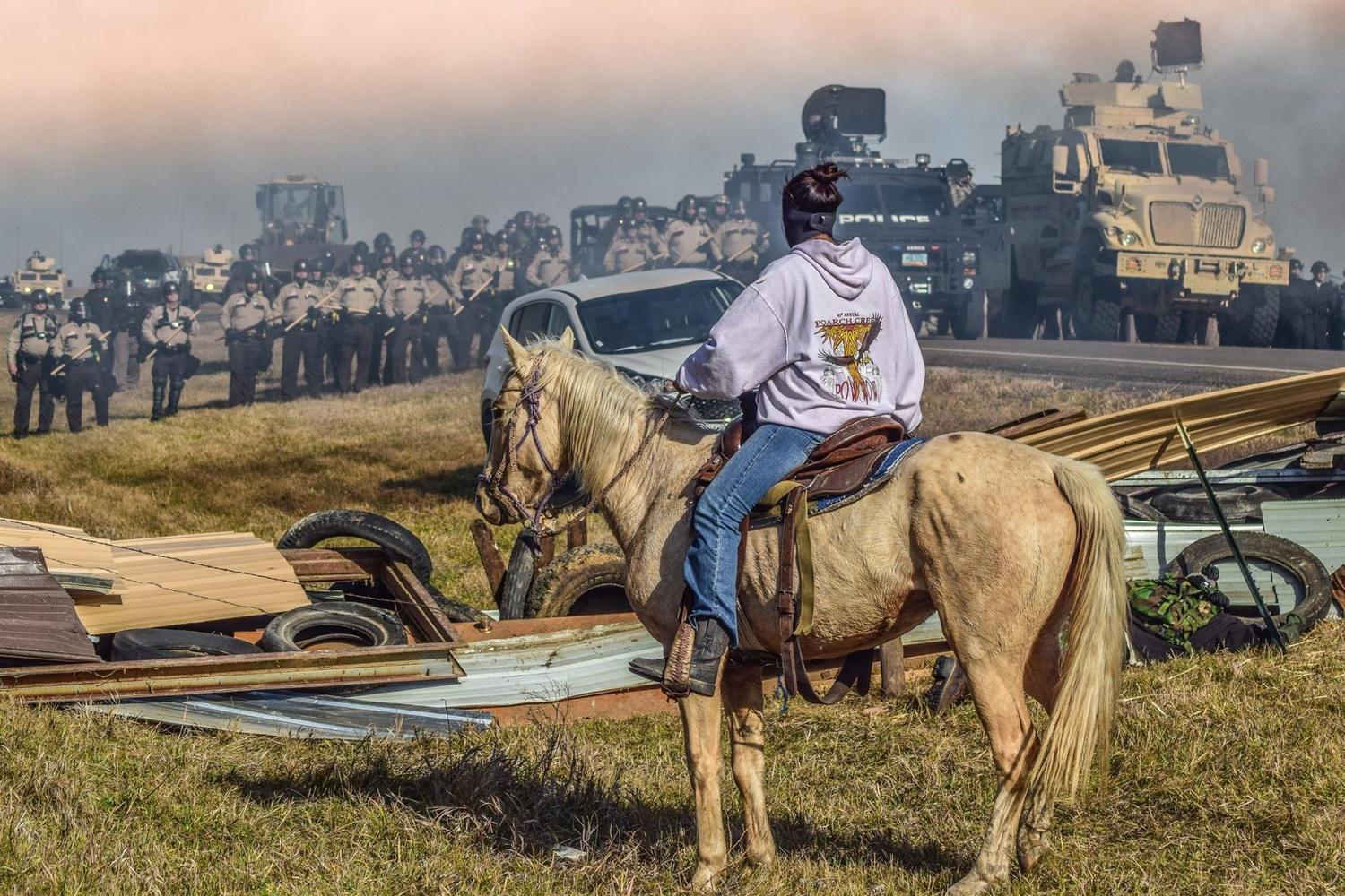 horseback indigenous American protestor faces militarized police at Standing Rock, North Dakota