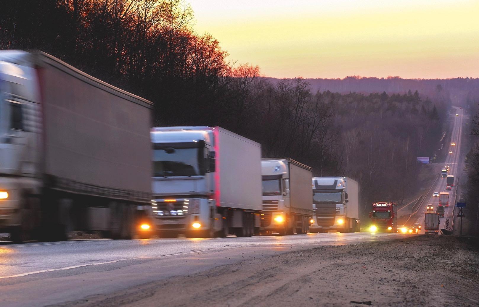 a line of trucks climbs a highway incline at dusk along a regional highway in the EU