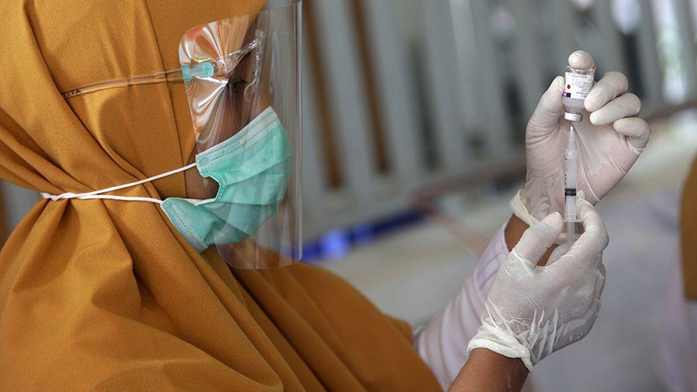 a masked, gloved woman prepares an injection