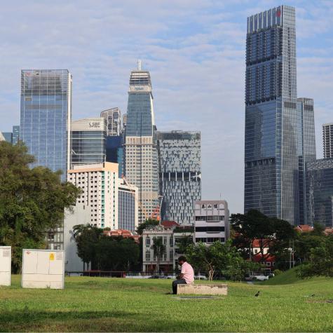 A migrant worker rests in a barren field against the backdrop of Singapore’s financial district.