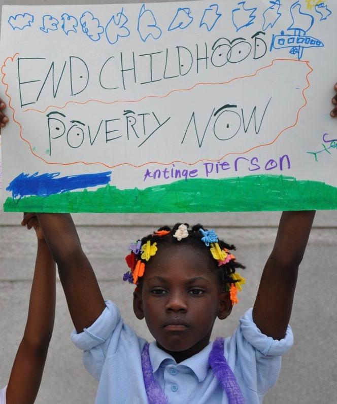 child holds up poster reading 'End Childhood Poverty Now'