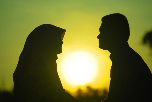 Face silhouettes of man and woman looking at each other agains sunset