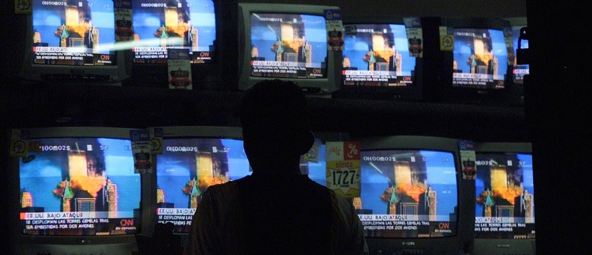 man stands before multiple television screens showing the burning Twin Towers of the WTC
