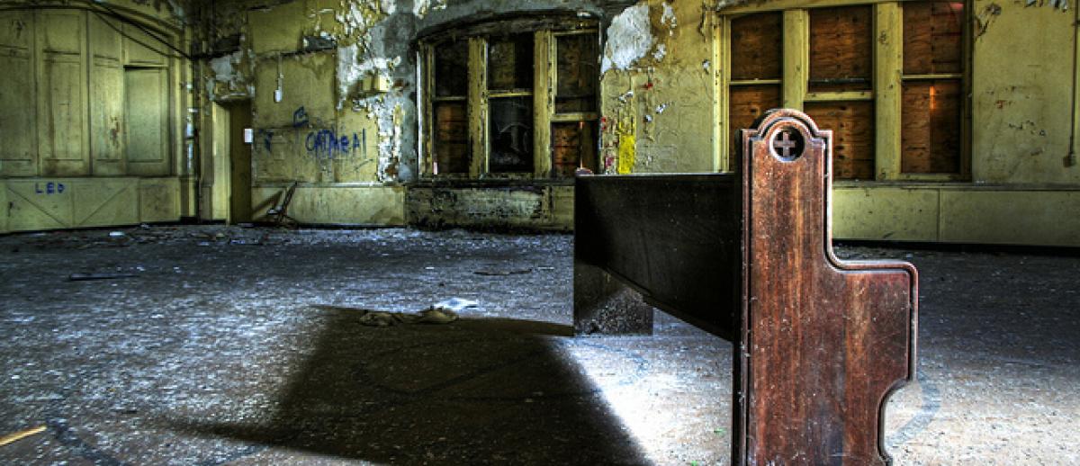 a single pew in a dilapidated boarded up church; image credit Chris Luckhardt