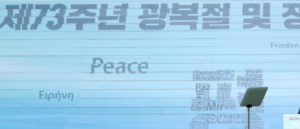 South Korean minister at conference podium with backdrop showing word Peace in numerous languages