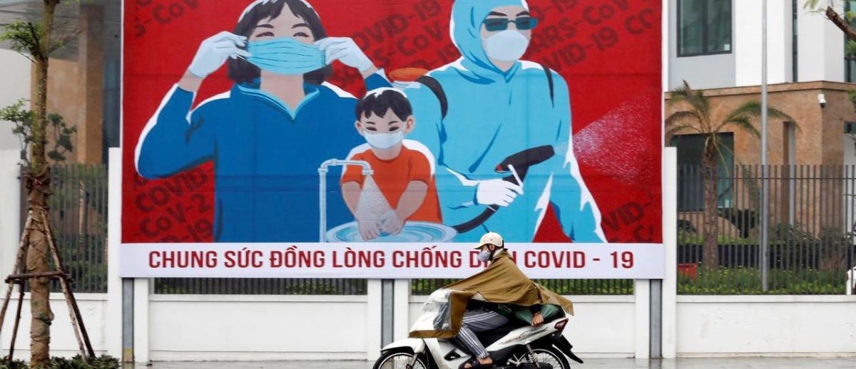 A man on a motorcycle drives past a Covid-19 fight poster in the capital city of Hanoi, Vietnam