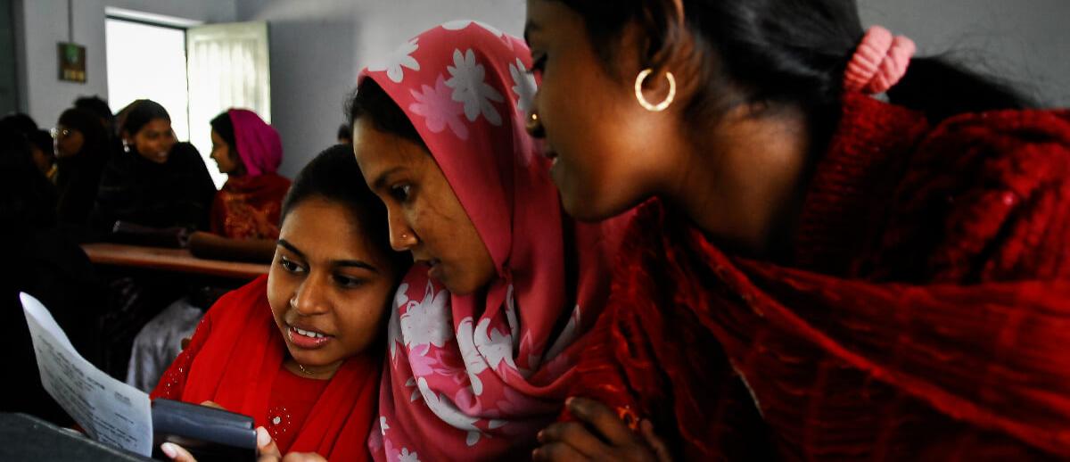 three South Asian women cluster around a smartphone