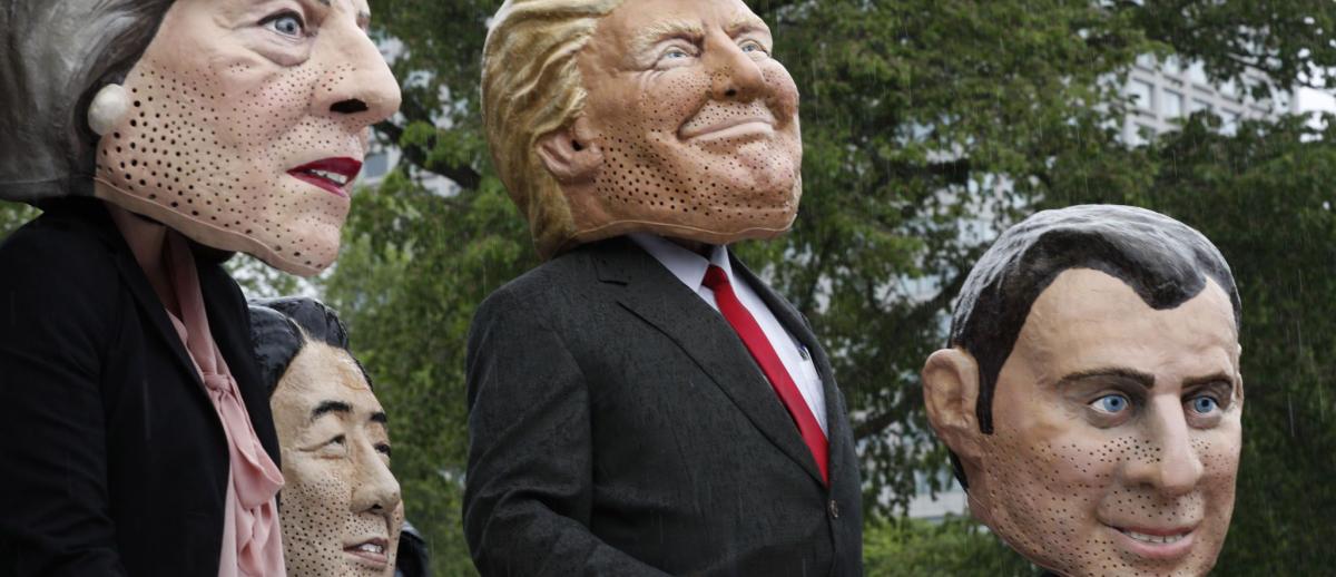 protesters in caricature masks of Teresa May, Shinzo Abe, Donald Trump, and Emmanuel Macron