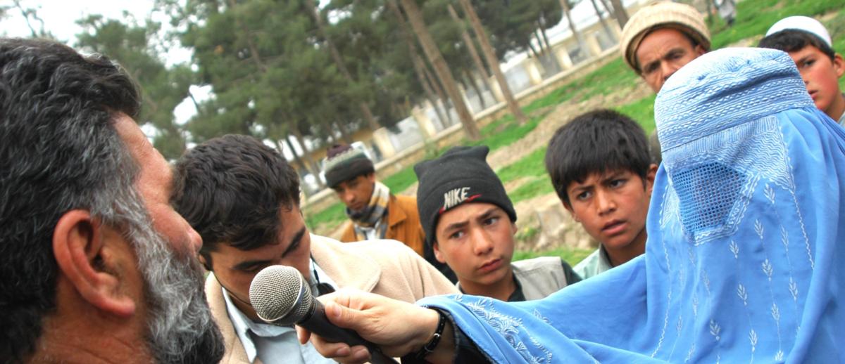 female Afghan journalist in chadri interviews a male subject