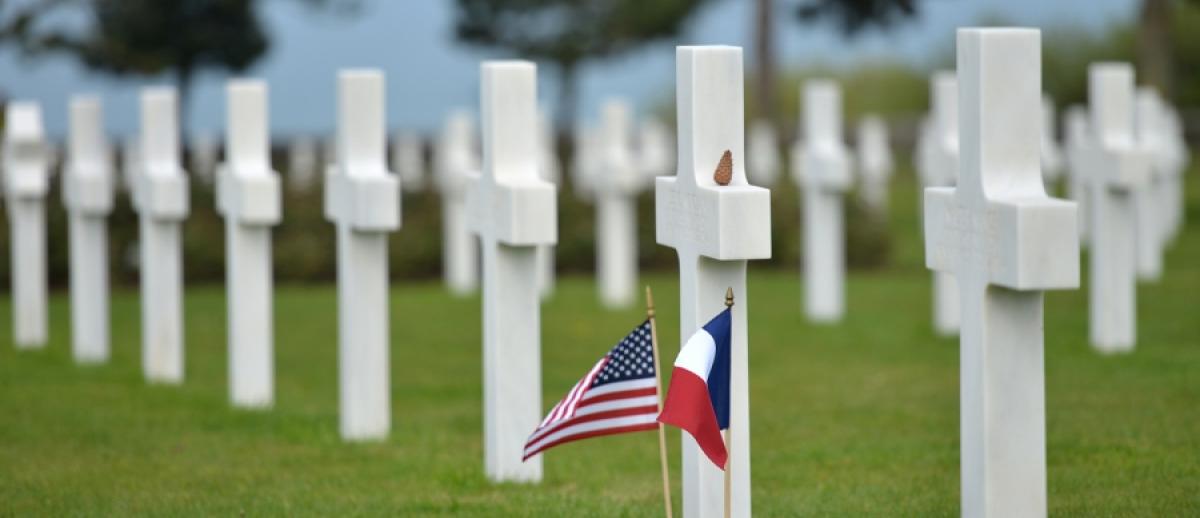 gravestones with US and French flags at the Normandy American Cemetery and Memorial in Colleville-sur-Mer, Normandy, France.