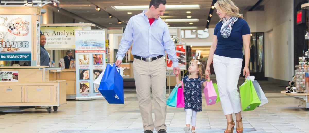 Dad, mom, and little girl holding hands inside a mall