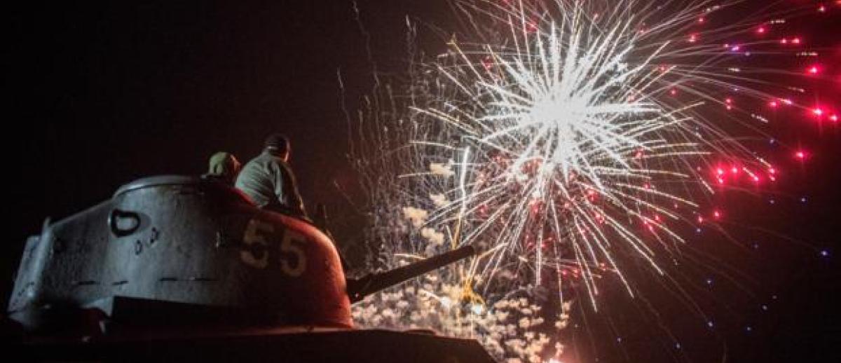 people seated on a WW2 Sherman tank watch firesworks in Normandy, France