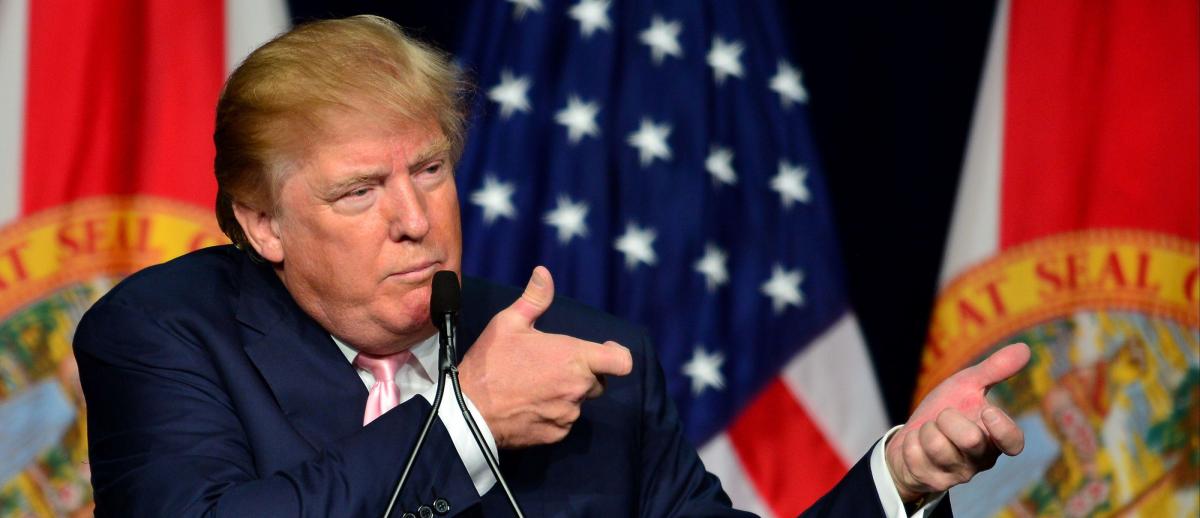 Donald Trump holding up his arms at public address in gesture of holding a rifle