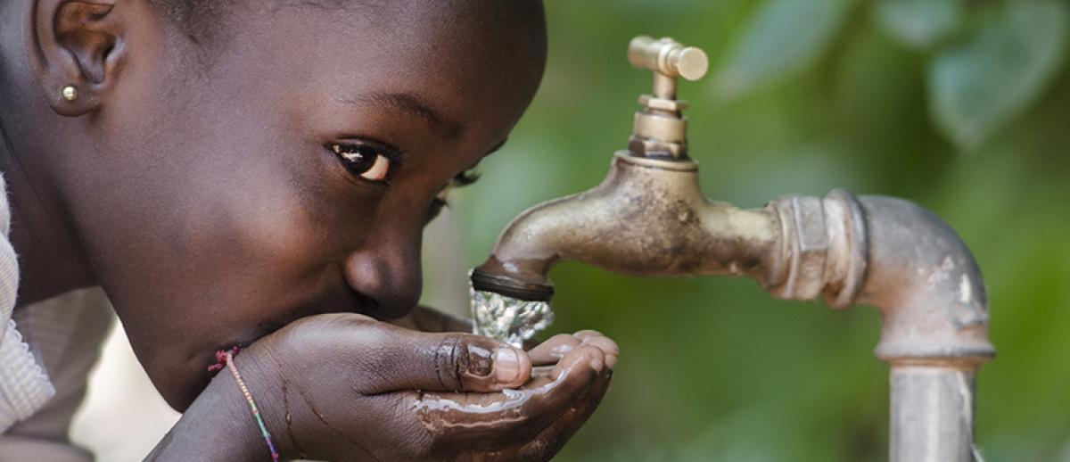 a girl cups hands to drink from an outdoor faucet