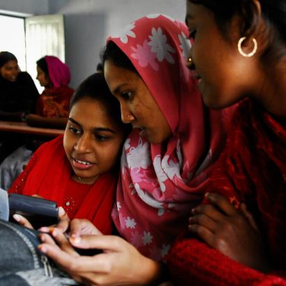 three South Asian women cluster around a smartphone