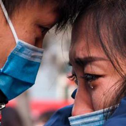 a man consoles a weeping woman, both wearing surgical masks