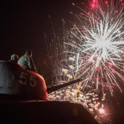 people seated on a WW2 Sherman tank watch firesworks in Normandy, France