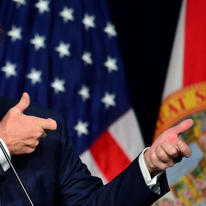 Donald Trump holding up his arms at public address in gesture of holding a rifle